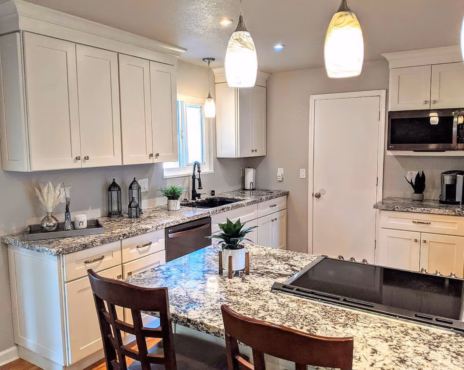Bright modern kitchen with white cabinets, granite counters, island, and pendant lights.
