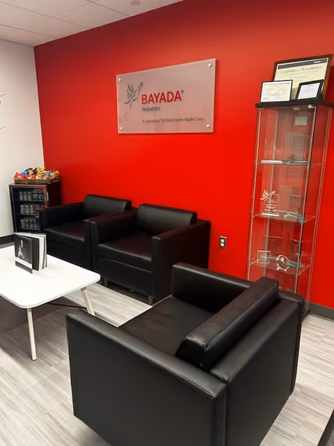 Modern waiting area with black leather chairs, red wall, and BAYADA Pediatrics sign.
