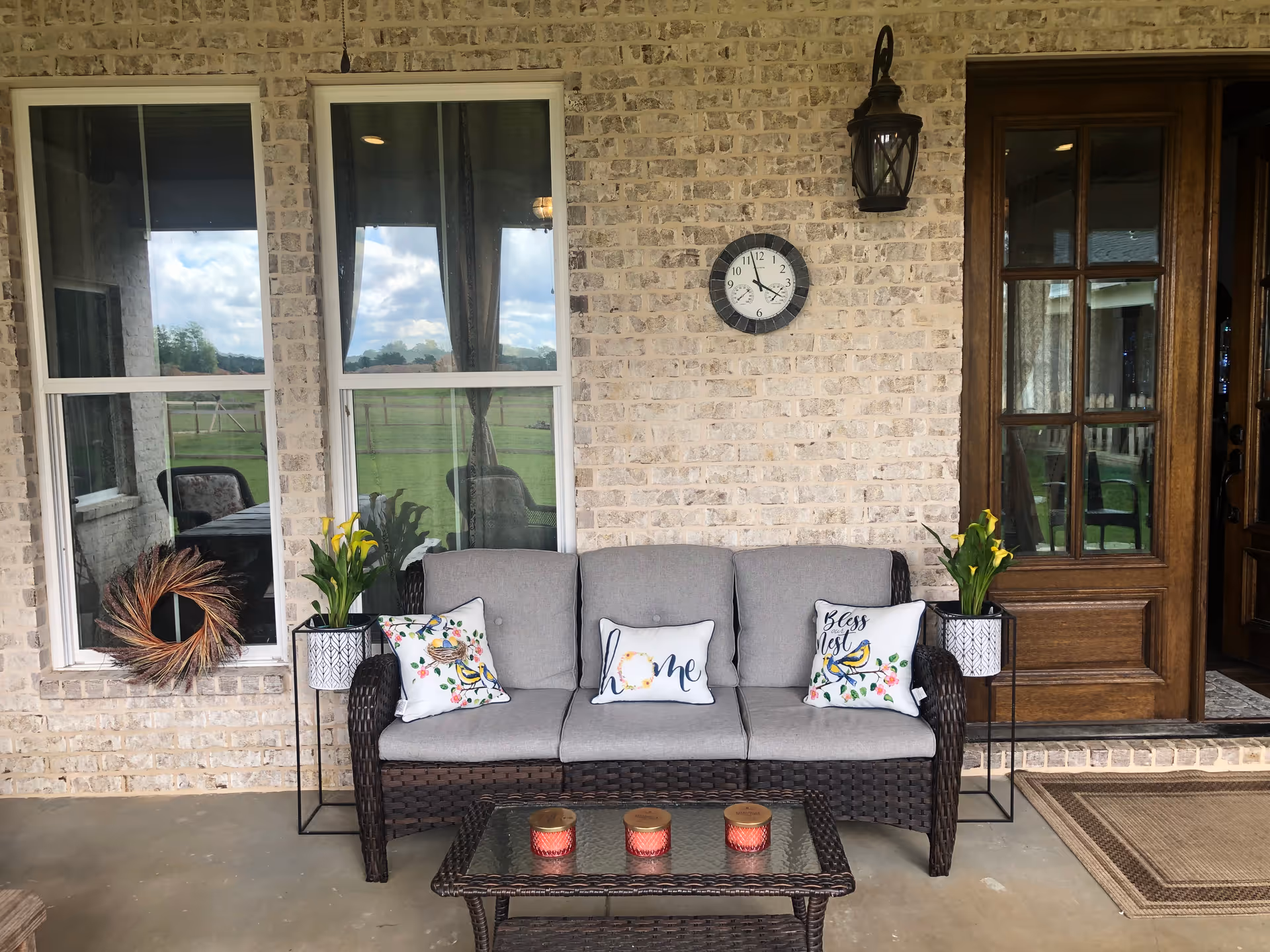 Patio seating area outside a brick house with a wicker sofa, plants, and a coffee table.