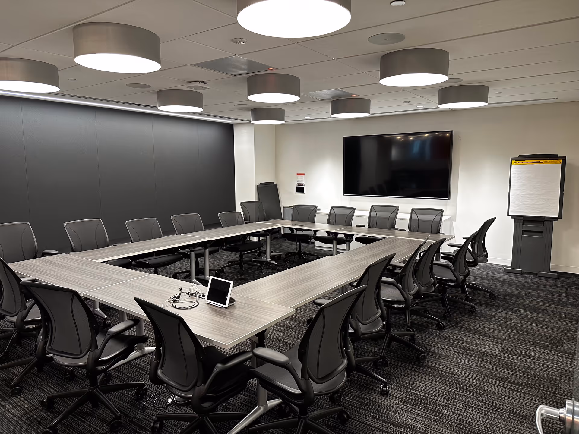 Large modern conference room with U-shaped table, chairs, and wall-mounted screen.