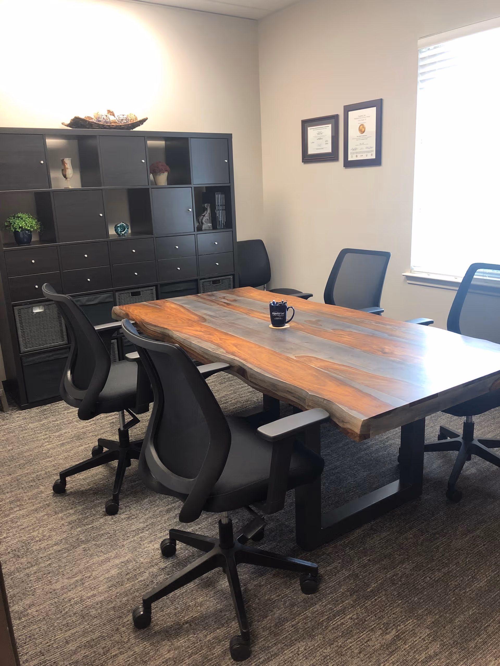 A modern conference room with a live-edge wooden table, black chairs, and shelving.