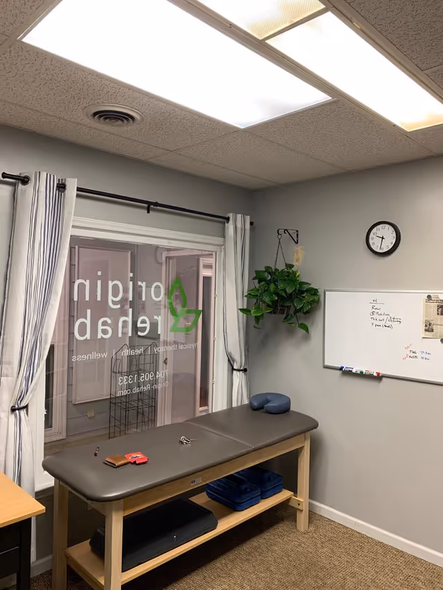 Therapy examination table in a small clinic room with a whiteboard and plant.