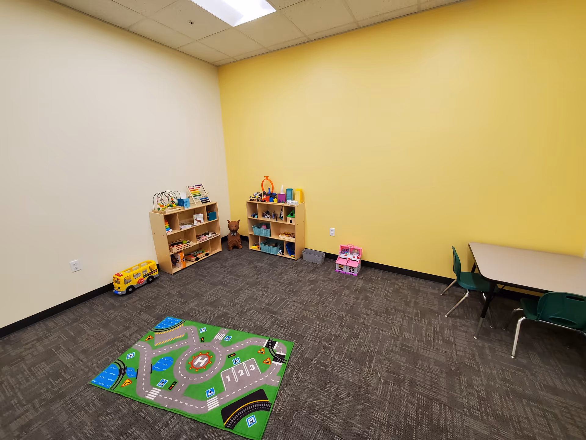 Bright playroom with yellow walls, toy shelves, and a colorful road-mat rug.