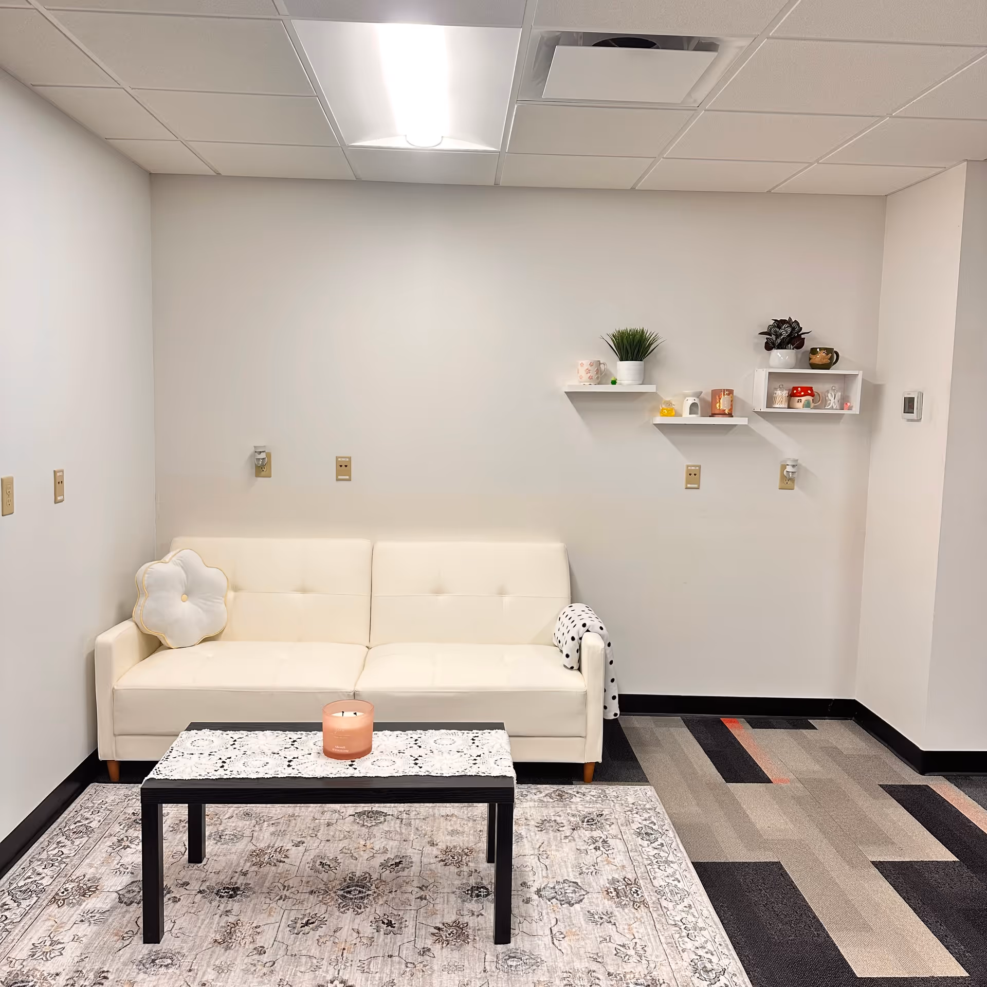 A modern white living area with sofa, coffee table, candle, and decorative shelves.
