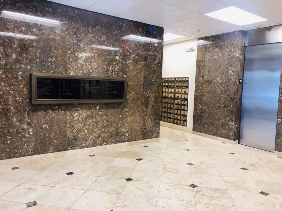 Marble lobby with directory panel, mailboxes, and an elevator along a hallway.