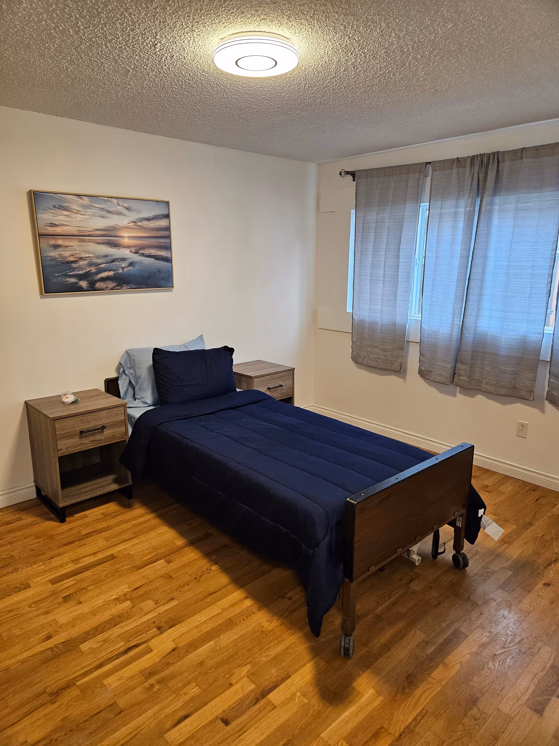 A small bedroom with a single bed, two nightstands, and a window with curtains.
