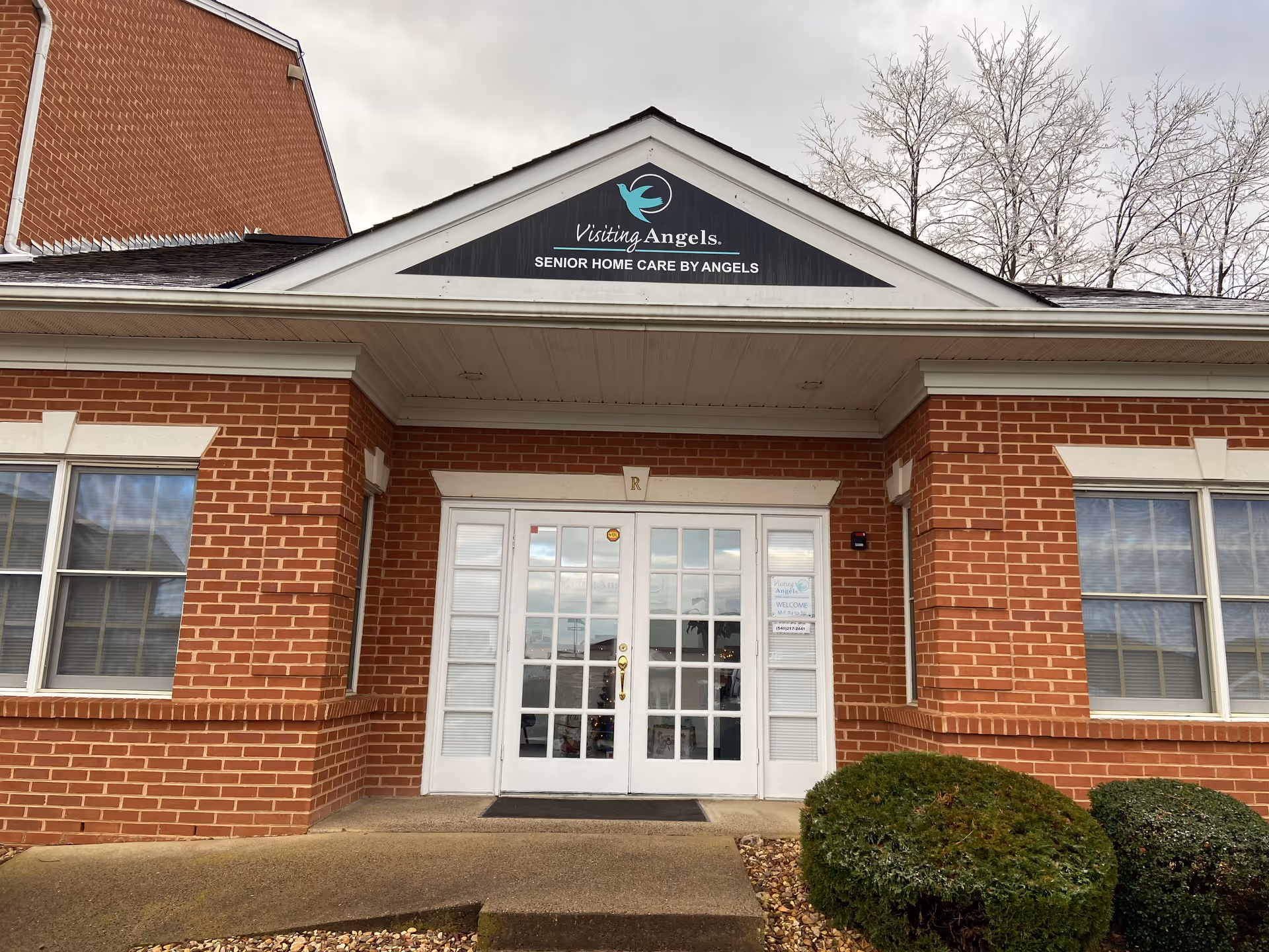 Brick building entrance with glass doors and a Visiting Angels sign above.