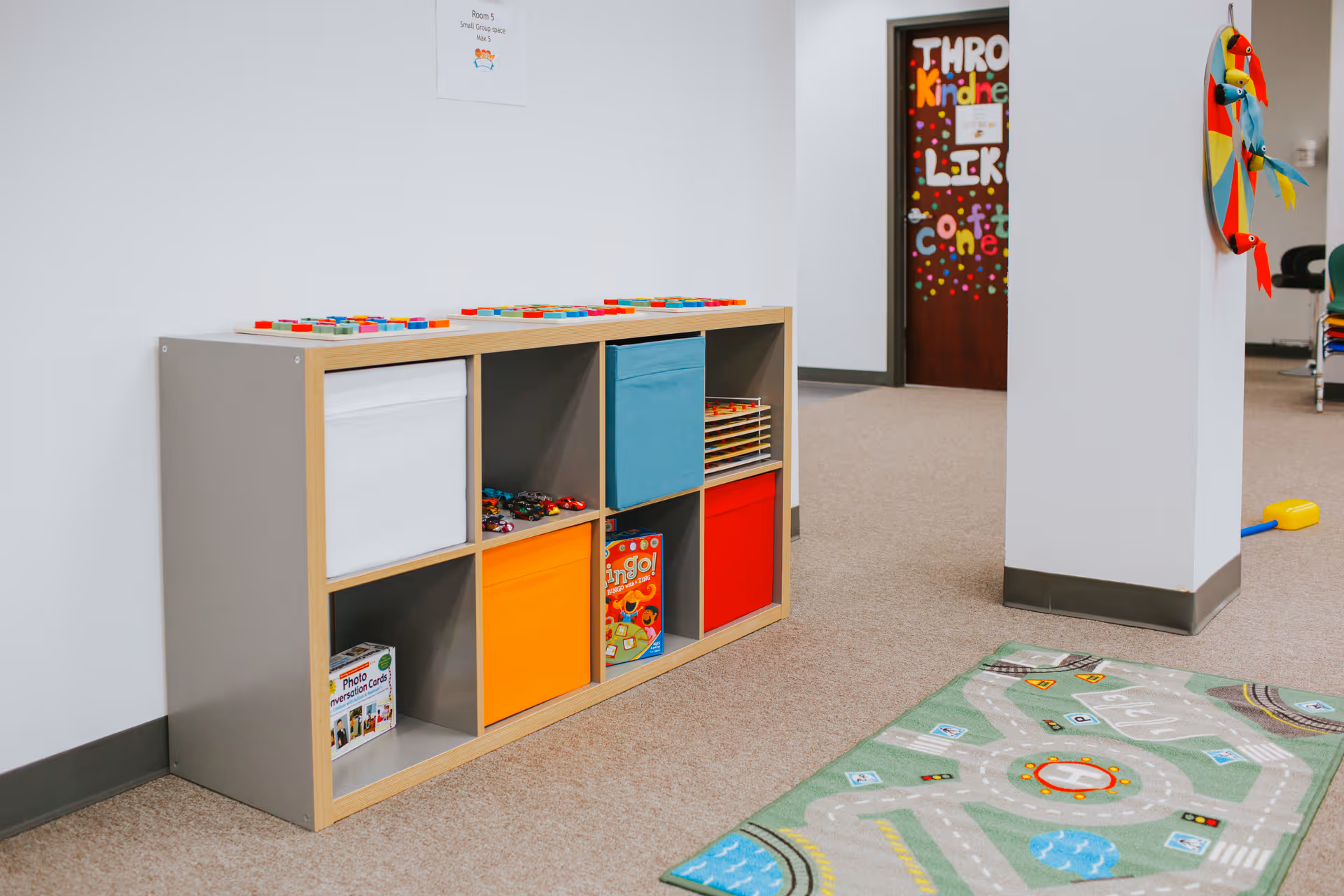 Colorful cubby shelves with bins and a play rug in a bright indoor activity room.