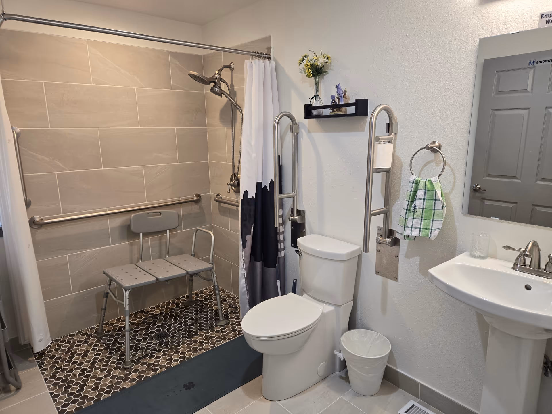 Accessible senior living bathroom with a shower bench, grab bars, toilet, and sink.