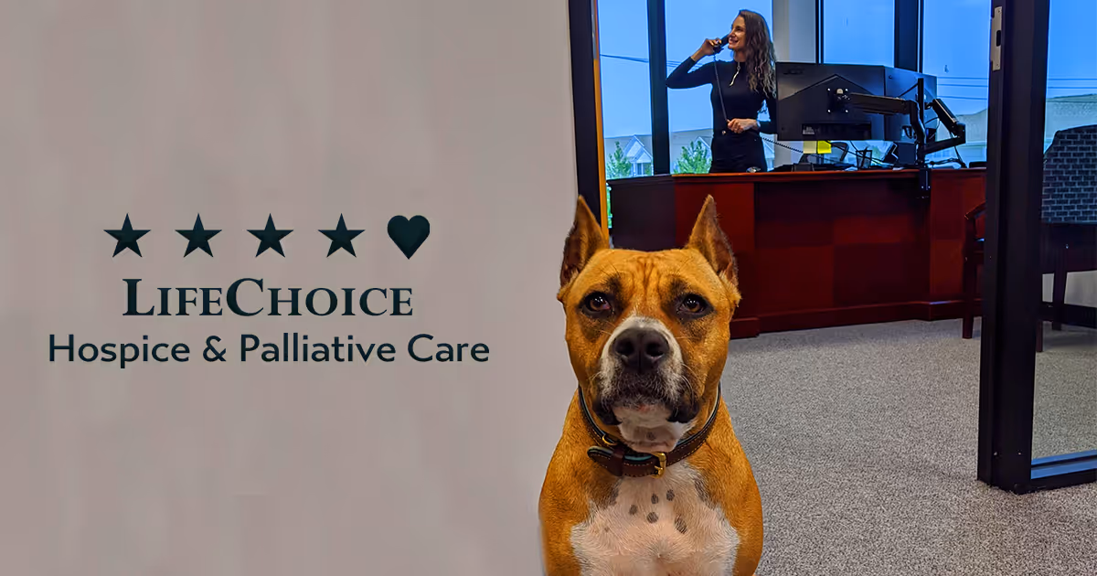 A dog sits in a reception lobby beside a LifeChoice Hospice sign and receptionist desk.