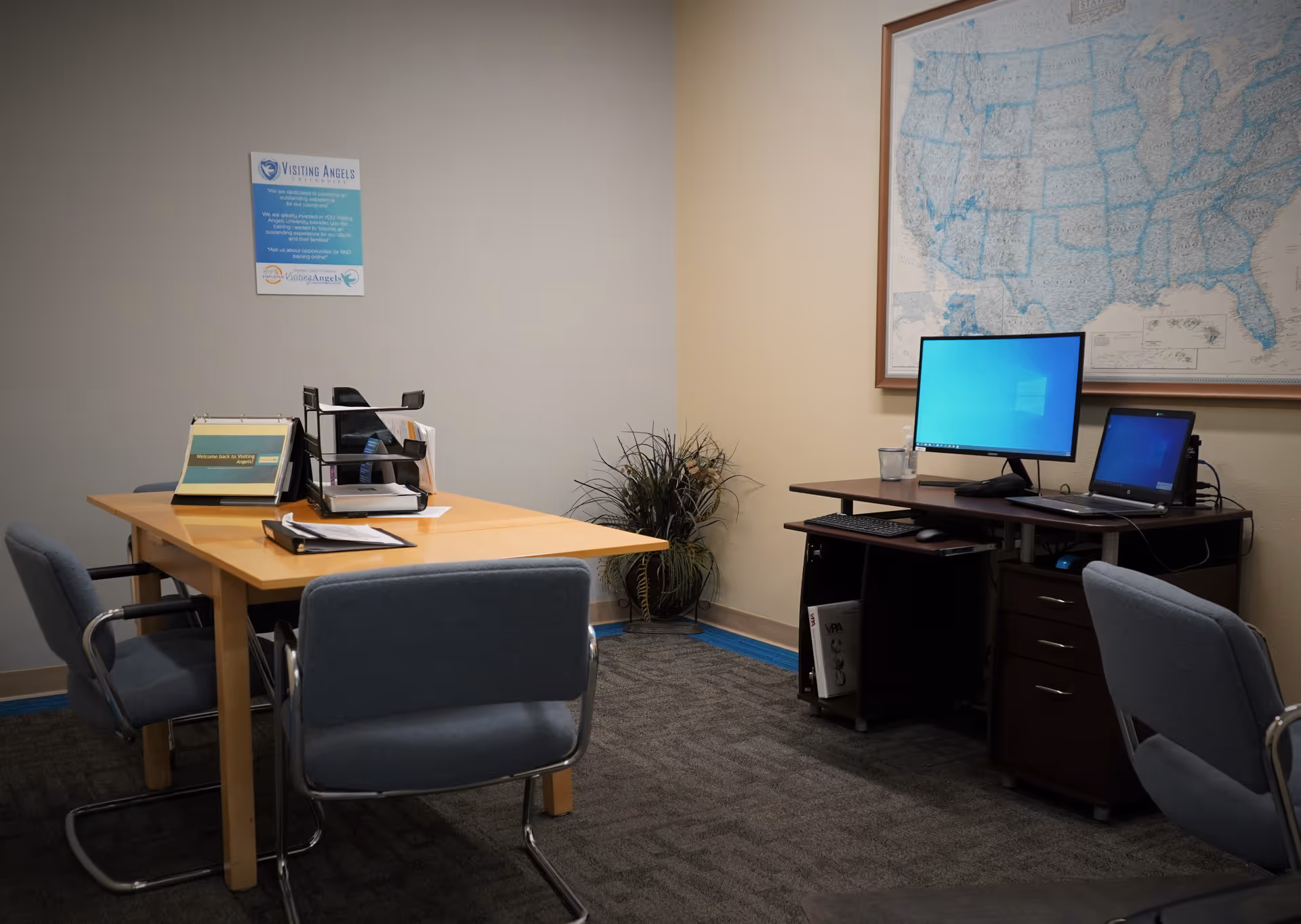 Office area with wooden table, two blue chairs, computer desk, and large map on wall.