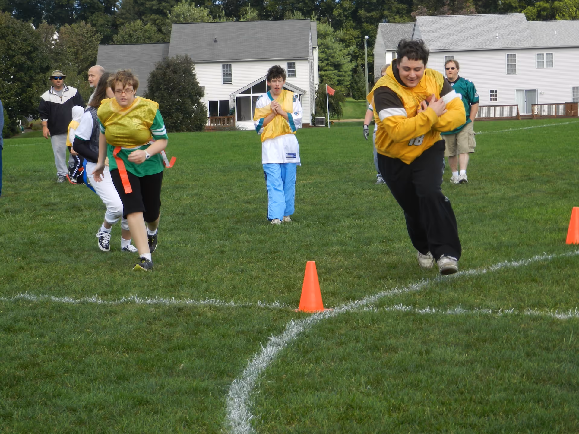 Group of people wearing colored vests sprint across a grassy field marked with cones.