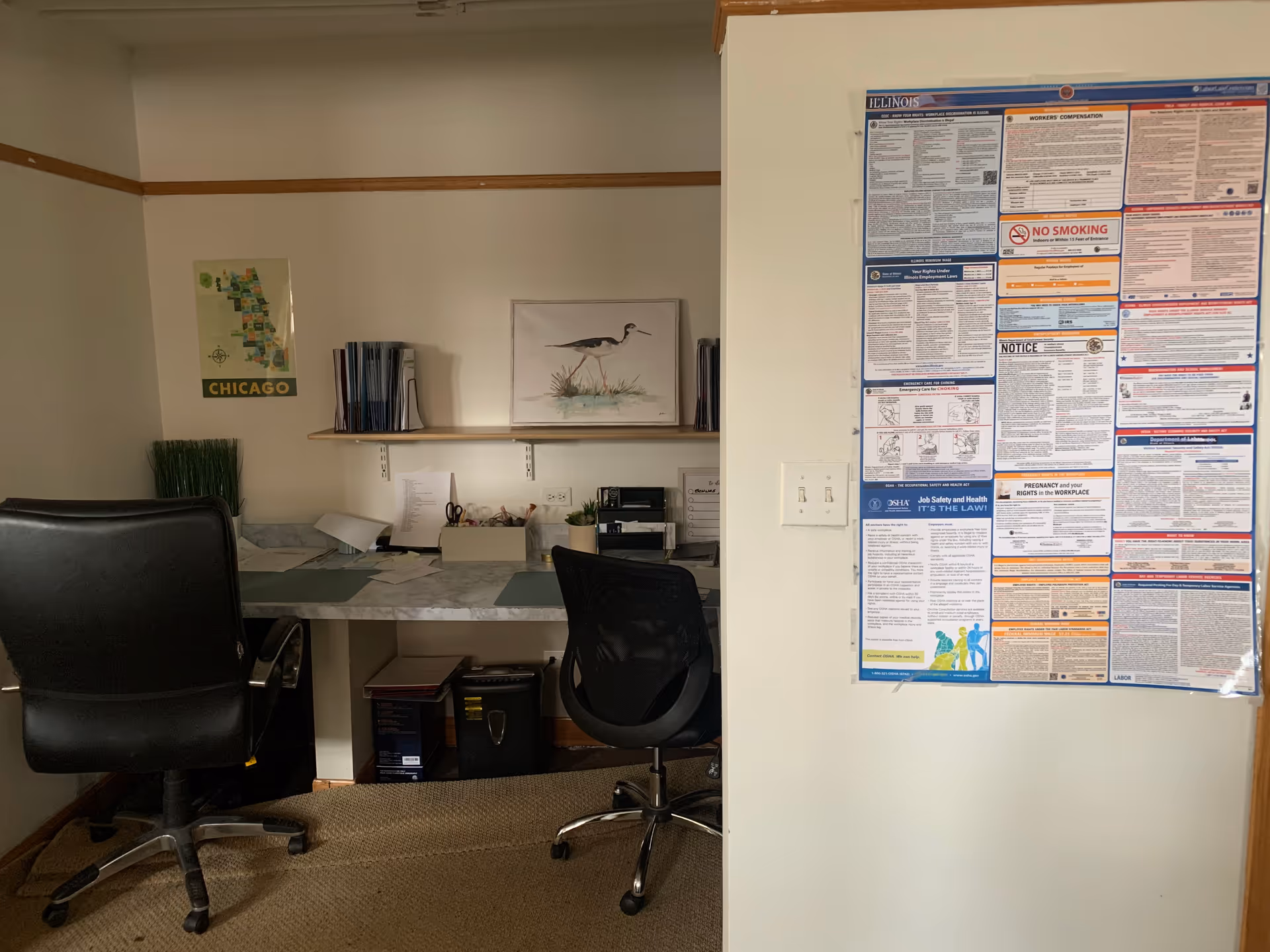 Office area with desks, chairs, shelves, wall poster, and large information board.