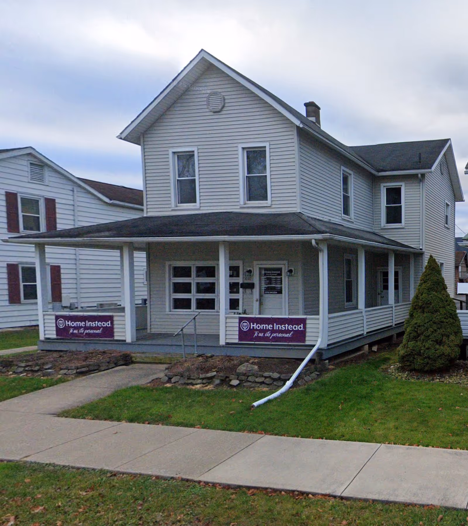 Two-story white building with a covered front porch and Home Instead signs.