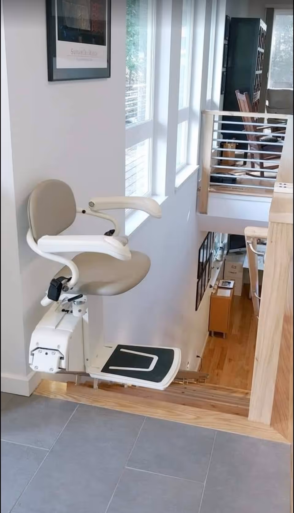 A stair lift chair mounted on a wall beside windows in a bright interior.