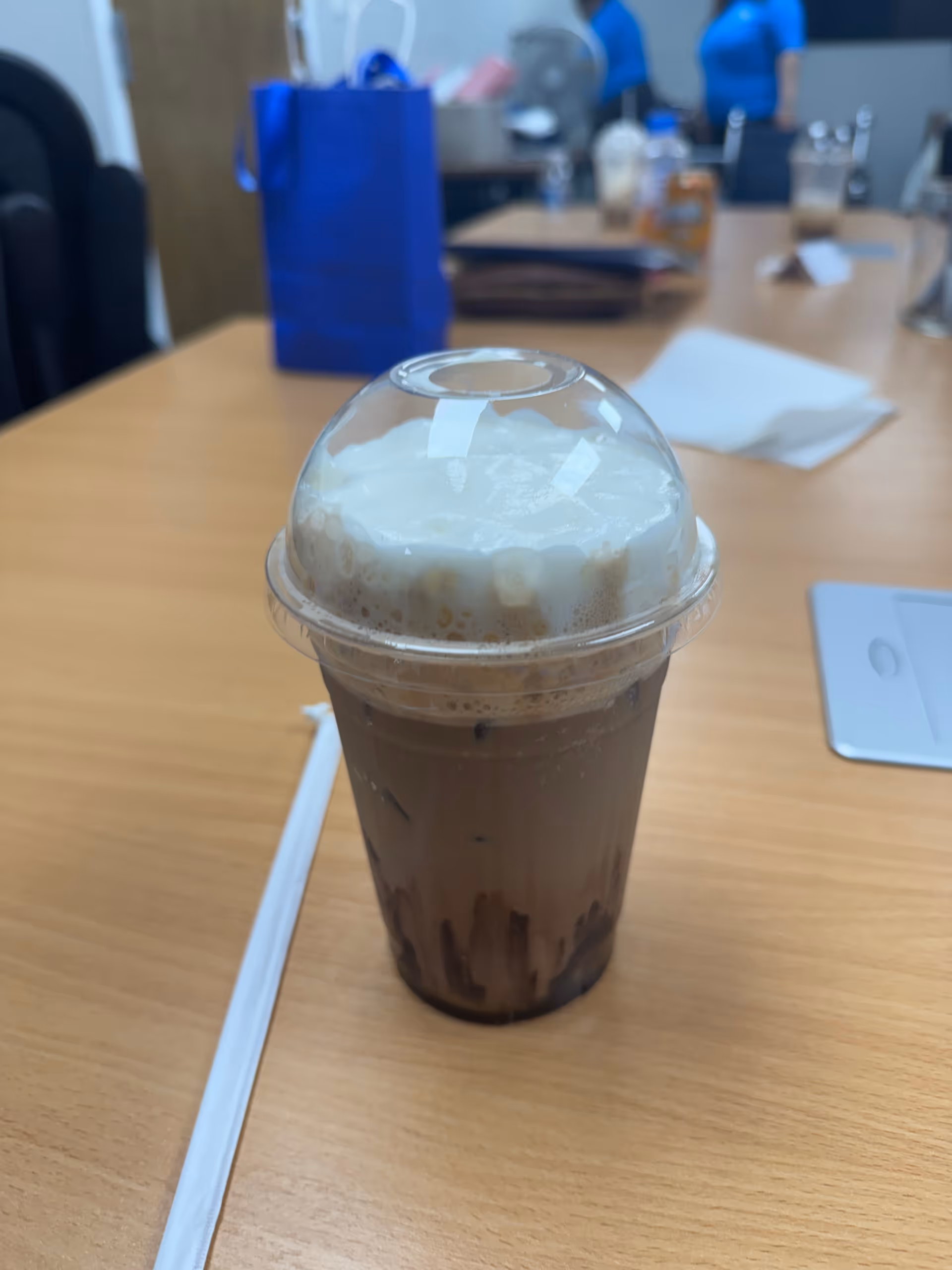 An iced coffee with whipped cream on a wooden table in a dining area.