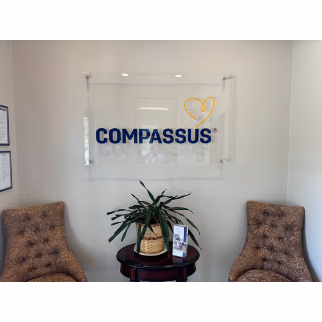 Lobby seating area with Compassus sign on the wall, two patterned chairs, and a plant table.